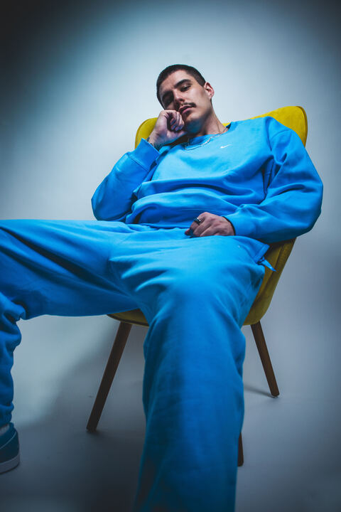 Person wearing a blue outfit sitting on a yellow chair against a gray background

